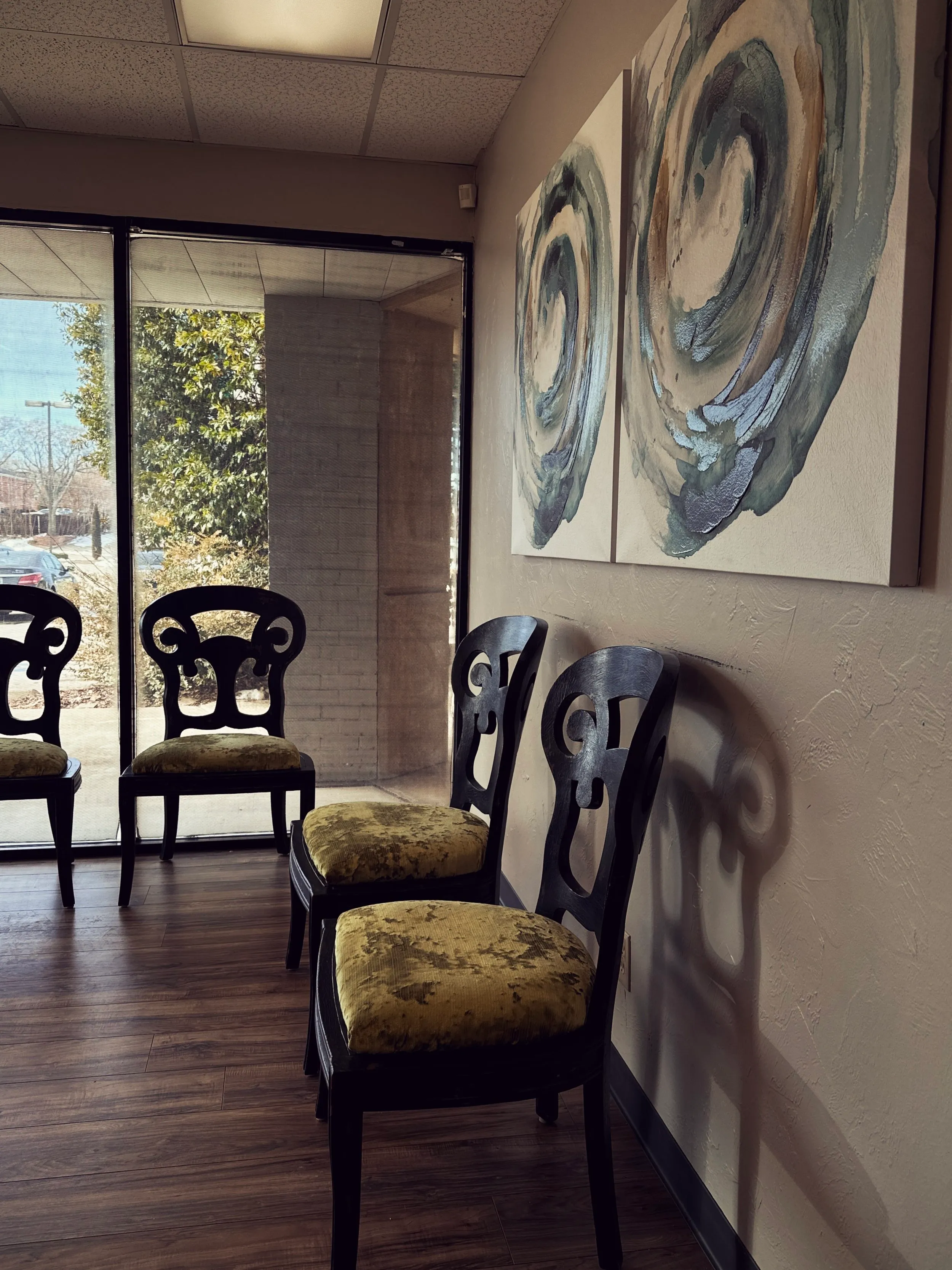 A waiting nook with antique gold-green velvet chairs and a pair of blue abstract paintings beside a sunlit window