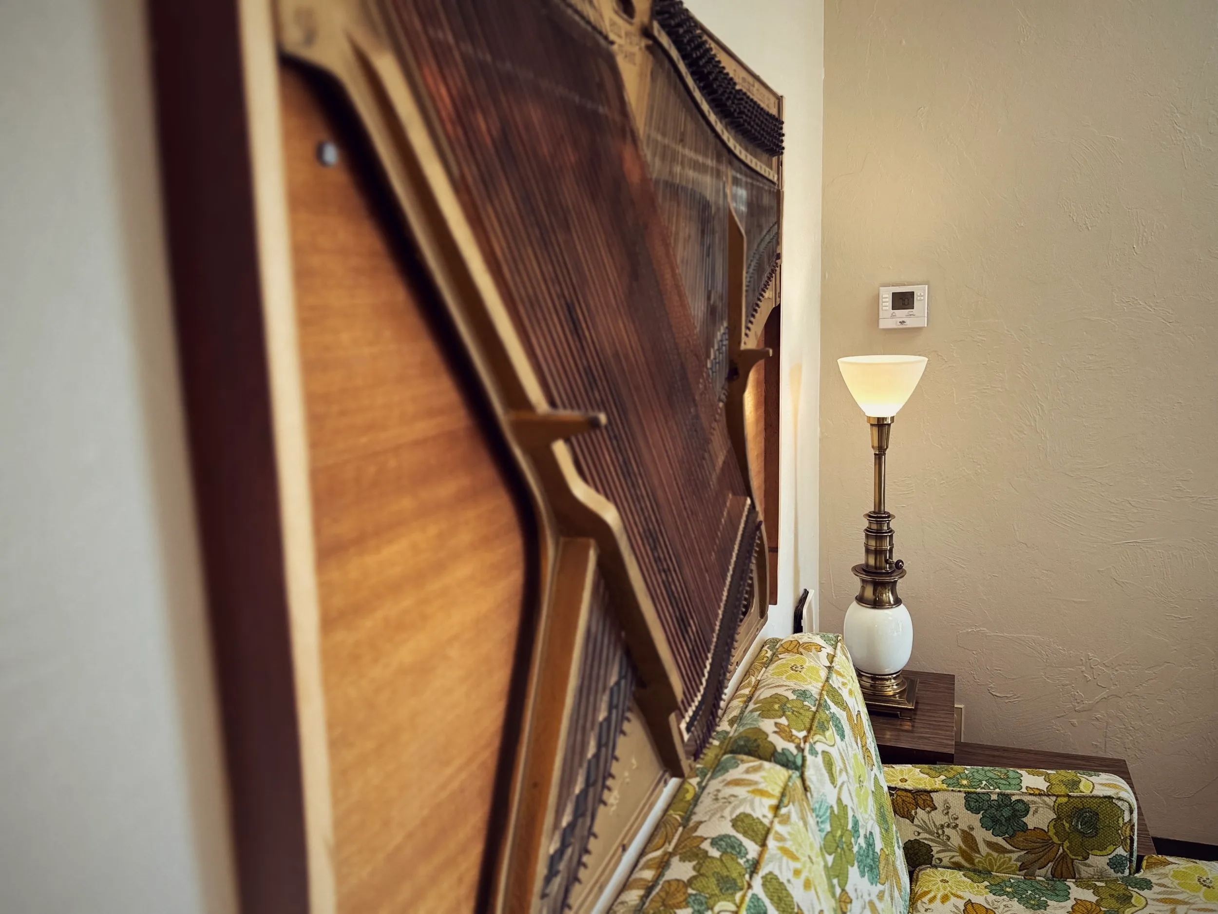 A cozy corner with a vintage upright piano, a glowing brass lamp, and a green floral sofa