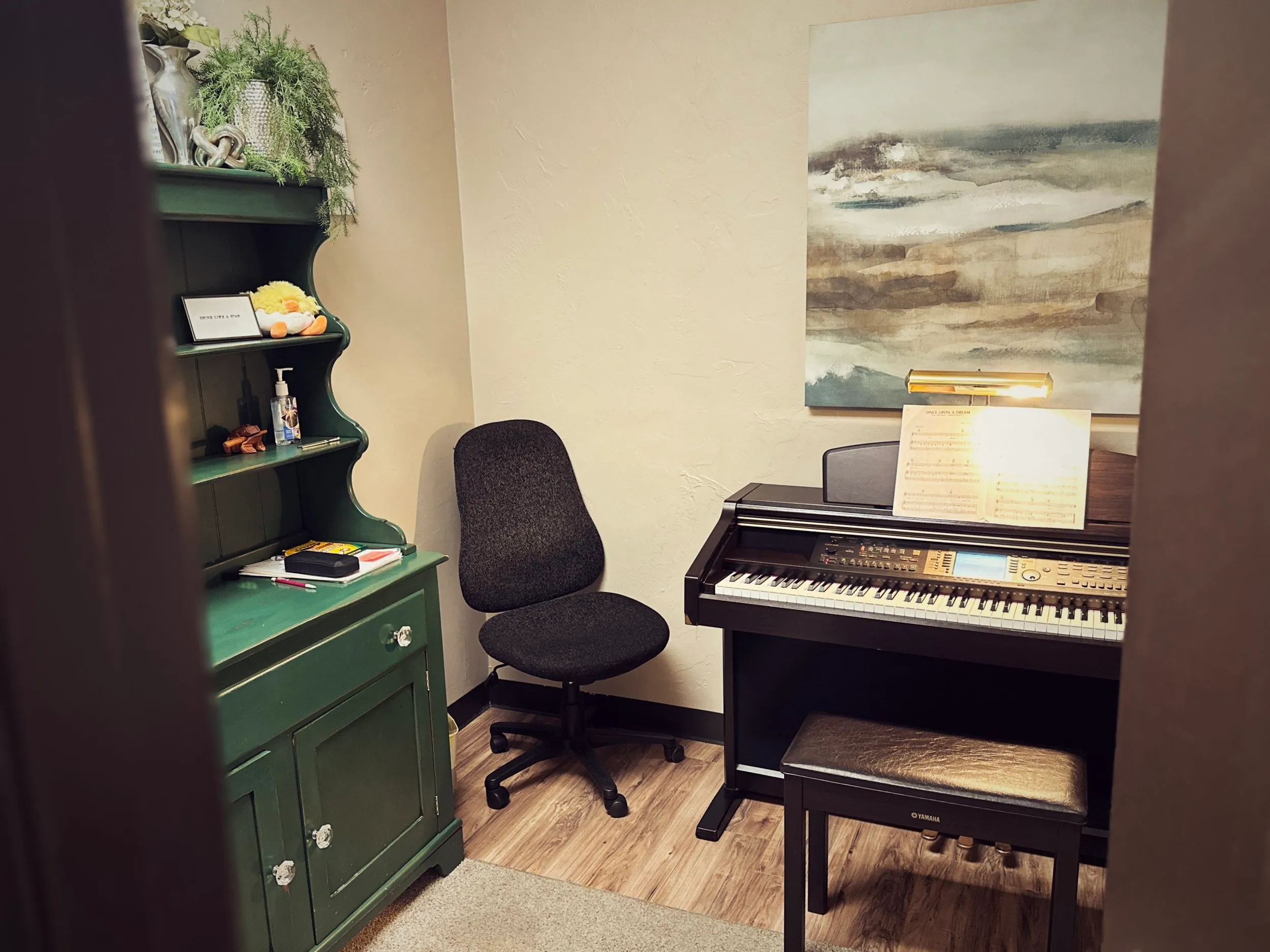 A piano lesson room with a green hutch, a digital piano, and a soft landscape painting