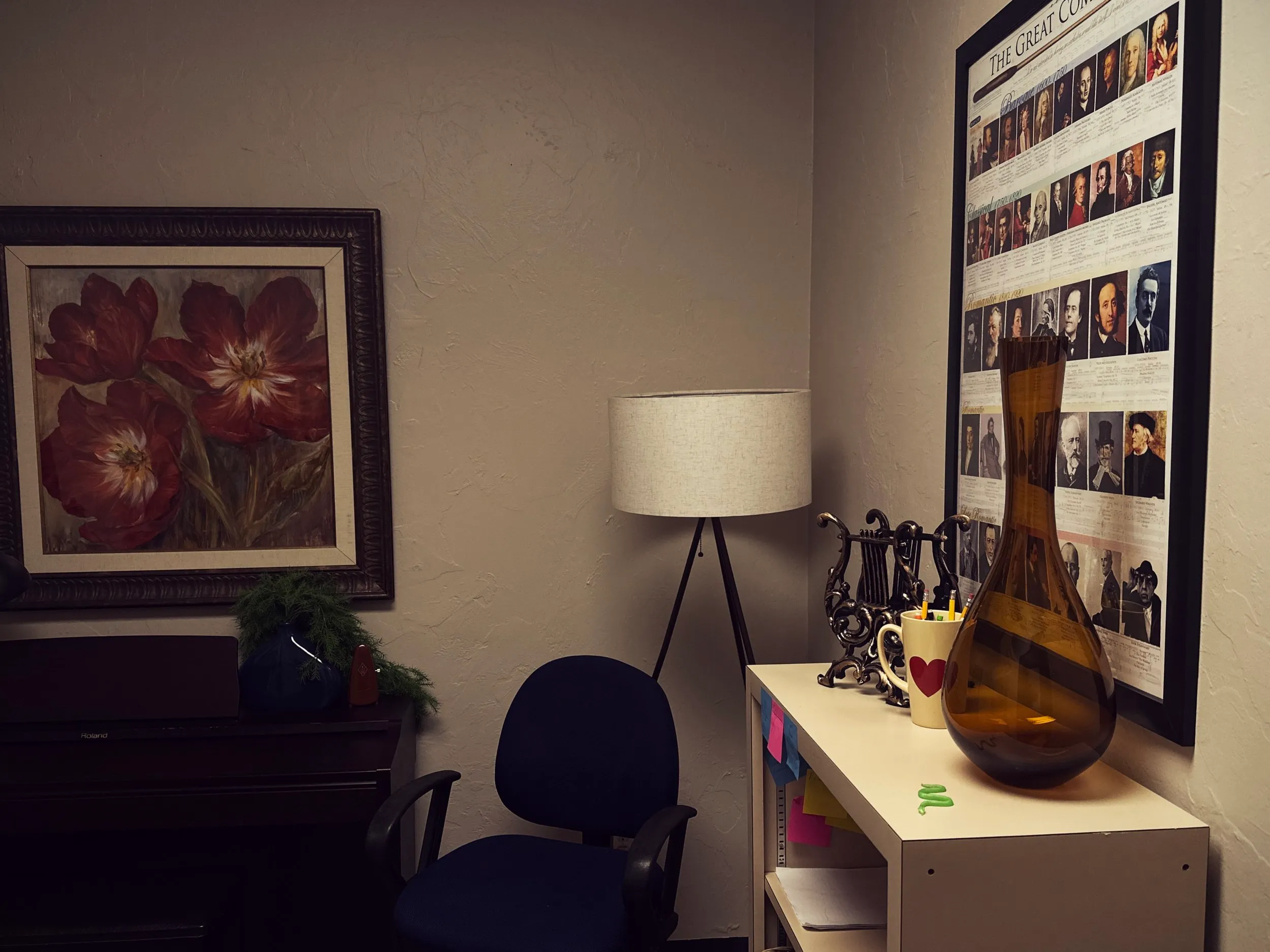 A lesson corner with a framed red-tulip painting, a tripod floor lamp, and a Great Composers poster above a piano